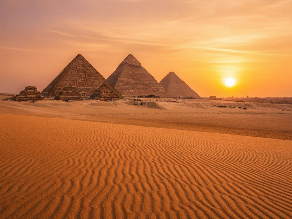 The Great Pyramids of Giza standing tall against golden desert sands at sunset.