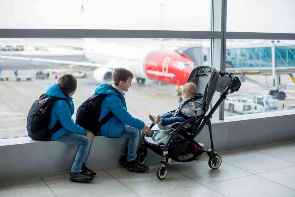 Prechool children with backpacks and their baby boy in stroller at the airport, going on holiday, family concept